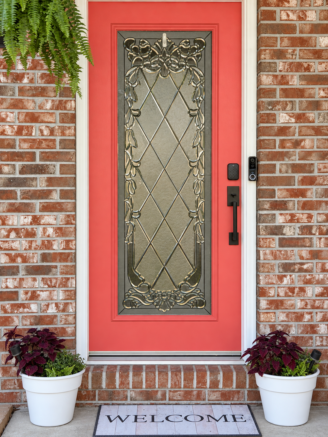 Vaasastays coral red front door with decorative glass, hanging fern, and welcome mat